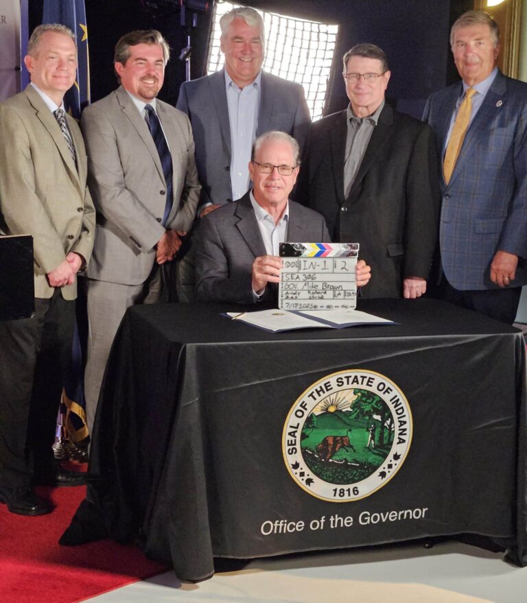 Gov. Mike Braun, seated, holds the clapperboard after the ceremonial signing of Senate Enrolled Act 306. Pictured with the governor are (from left) Robert Pepper, president of Huntington University, Richard Strick, mayor of Huntington, state Sen. Andy Zay, Bill Konyha, president and CEO of the Regional Chamber of Northeast Indiana, and state Rep. Dave Heine. (Photo/Marilyn Odendahl) 