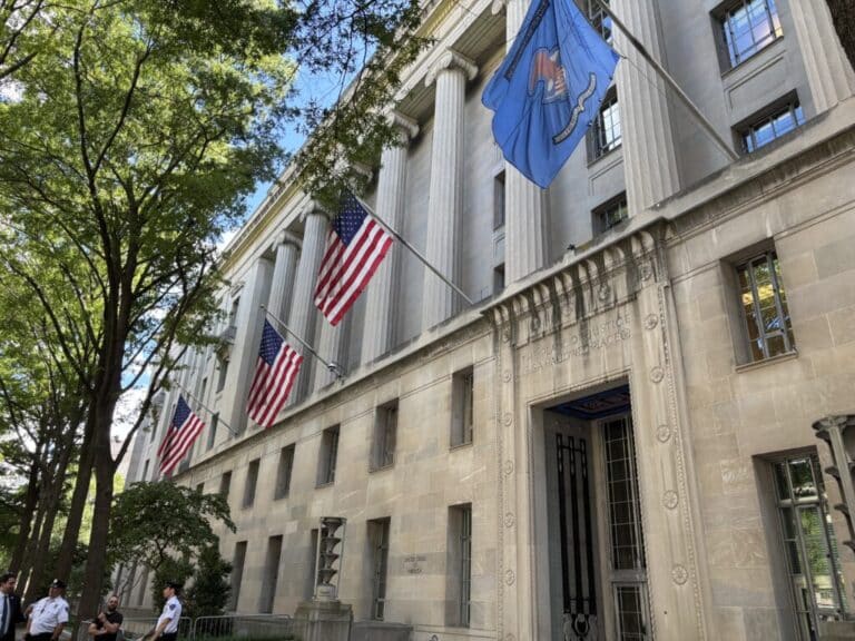 American flags hang alongside the official agency flag at the U.S. Department of Justice building in Washington, D.C., in August. The Justice Department is sharing state voter roll data with the U.S. Department of Homeland Security. (Photo/Jonathan Shorman of Stateline)